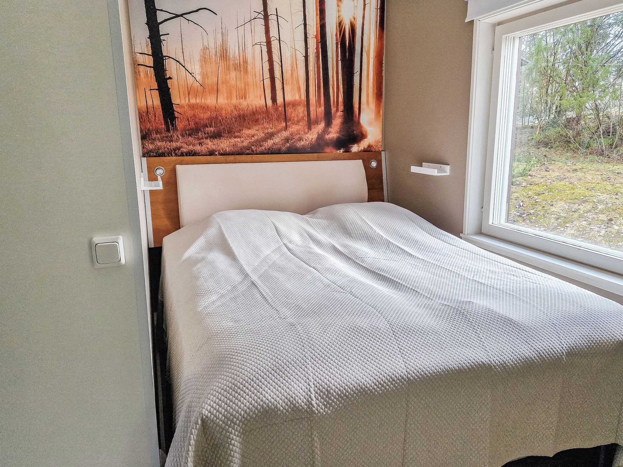 Une chambre à coucher avec un lit, une fenêtre et un tableau représentant une scène de forêt.
