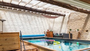 Une piscine intérieure dotée d’une terrasse en bois, de murs en pierre et d’un toit en verre.