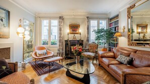 A spacious living room with a leather sofa, a glass coffee table, and a fireplace. There are bookshelves and a large mirror on the walls. - Triumphant Design, by Veeve (Paris)