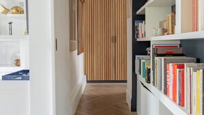 Ein Flur mit Fischgrätparkett, weißen Wänden und einem Bücherregal voller Bücher.