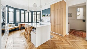 A modern kitchen with a central island, wooden flooring, and a built-in bench seating area. - A Vision in White, by Veeve (Paris)