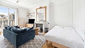 A bedroom with a bed, a blue sofa, a fireplace, a mirror, and a view of the city. - A Vision in White, by Veeve (Paris)