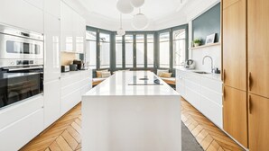 A modern kitchen with white cabinetry, a central island, and a large window providing natural light. - A Vision in White, by Veeve (Paris)