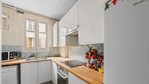 A modern kitchen with white cabinets, a wooden countertop, and a tiled backsplash. - Batignolles Gem, by Veeve (Paris)
