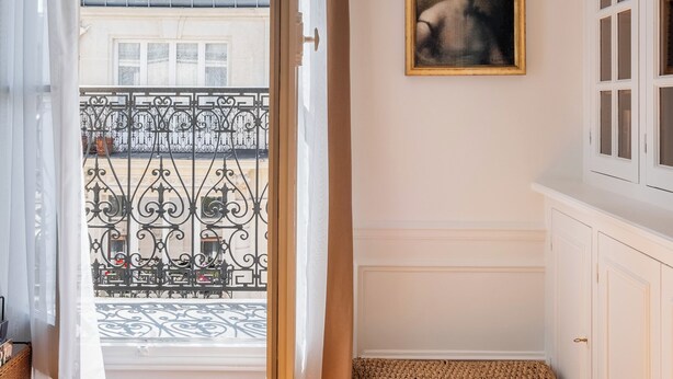 A room with a large window, a balcony with a wrought iron railing, and two framed portraits on the wall. - Literary Radiance, by Veeve (Paris)