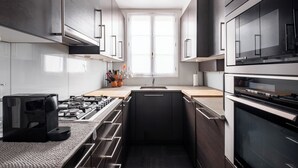 A modern kitchen with dark cabinetry, a built-in oven, and a window providing natural light. - Literary Radiance, by Veeve (Paris)