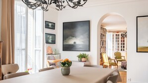 A dining area with a table set for six, a vase with flowers, and a bookshelf in the background. - Literary Radiance, by Veeve (Paris)