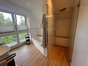 Ein modernes Badezimmer mit einer Duschkabine, einer Badewanne und einem Fenster mit Blick auf Grünflächen.