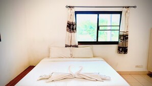 Uma cama bem arrumada com uma toalha em formato de cisne, uma janela com cortinas e uma parede lisa.