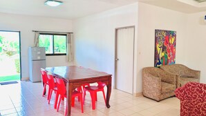Uma sala de estar ampla com uma mesa de jantar de madeira e cadeiras vermelhas, um sofá e um quadro abstrato colorido na parede.