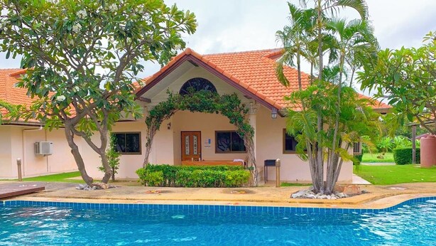 Uma casa com piscina, cercada por vegetação e palmeiras.