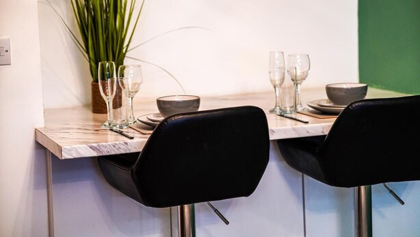 A dining area with a marble countertop, black chairs, and a potted plant. - 40percent off Monthly /2 Bedroom apt / City Centre (Swindon)