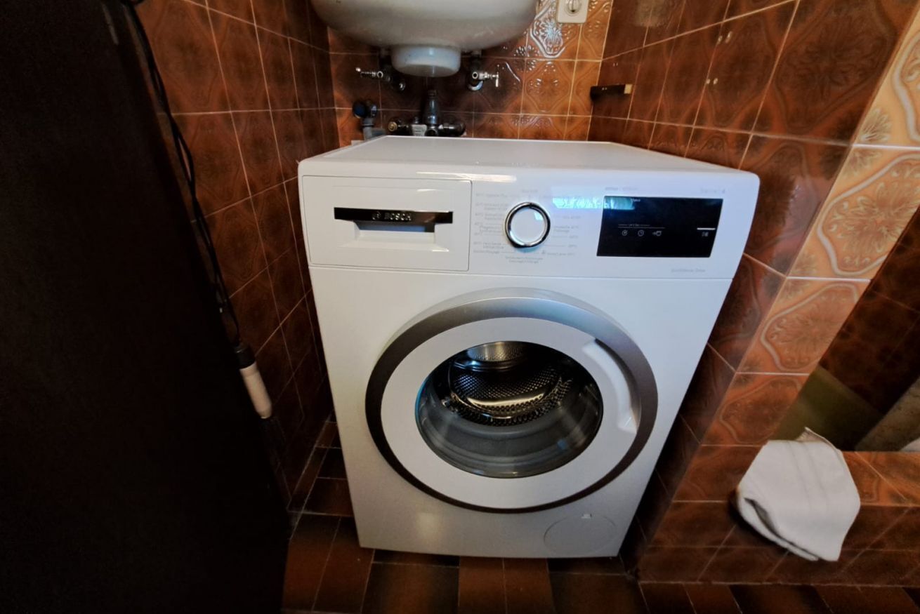 A compact, modern front-loading washing machine in a bathroom with brown patterned tiles.