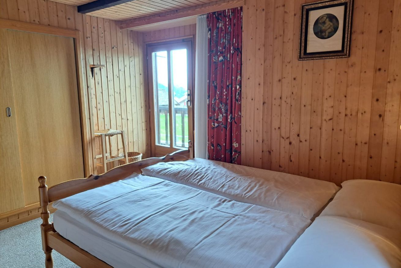A wooden room with a bed, a door, and a window with curtains.