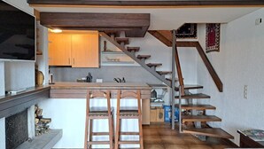 Eine kleine Küche mit einer zentralen Kochinsel, Holzstühlen und einer Treppe, die zu einem Schlafbereich führt.
