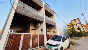 Un immeuble moderne à deux étages, doté d’un balcon, d’une entrée sécurisée et d’une voiture blanche garée devant.