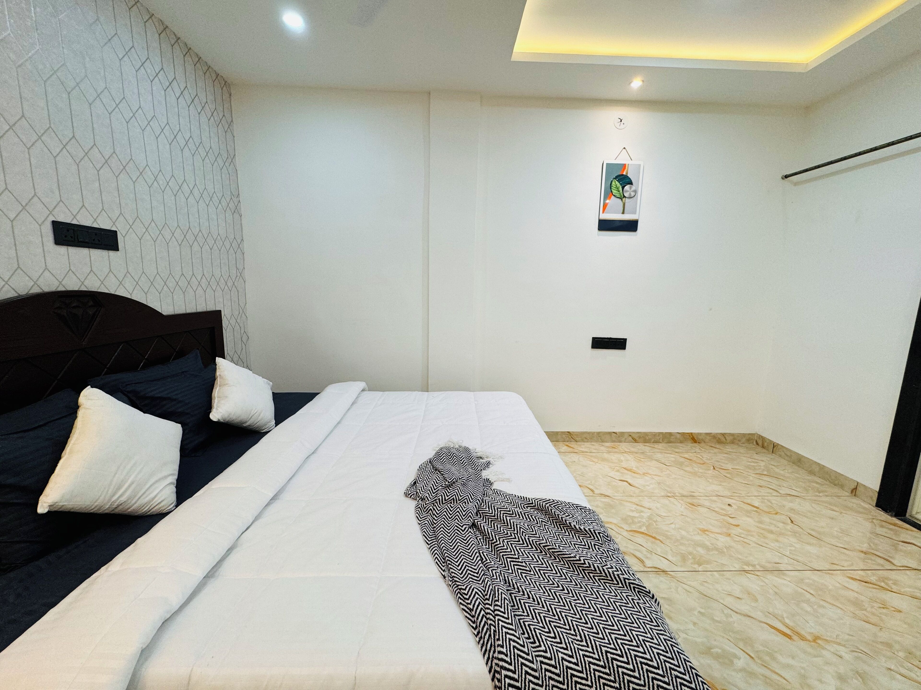A neatly made bed with a patterned throw, a headboard, and a wall with a geometric pattern.