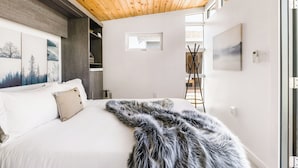Un dormitorio moderno con techo de madera, una cama grande con ropa blanca, un plaid de piel y obras de arte en las paredes.