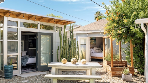 Una casa moderna con un patio, una pérgola de madera y un jardín con cactus y una palmera.