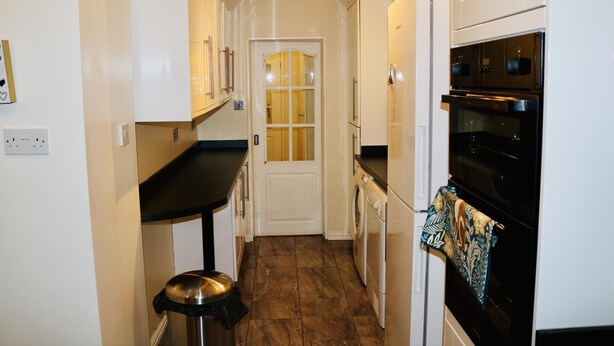 A compact kitchen with white cabinets, a black countertop, a stainless steel trash can, and a black oven.