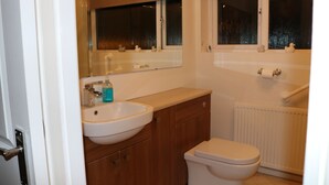 A bathroom with a white sink, wooden cabinets, a toilet, and a window with a view of the outside.