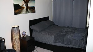 A bedroom with a bed, a nightstand, a lamp, and a painting on the wall.