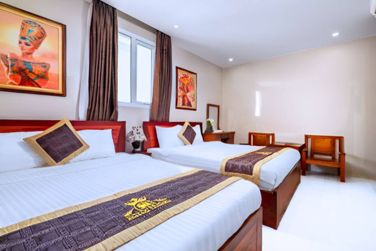 A hotel room with two beds, a desk, and a chair. There are curtains, a painting, and a window.