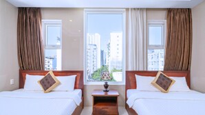 A hotel room with two beds, a nightstand, a window with curtains, and a view of buildings outside. - Dubai Hotel (Da Nang)