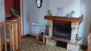 Una sala de estar con chimenea, piso de madera, puerta roja y un espejo en la pared.