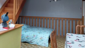 Un dormitorio con una cama alta, un escritorio con silla, una mesita pequeña y una colcha estampada.
