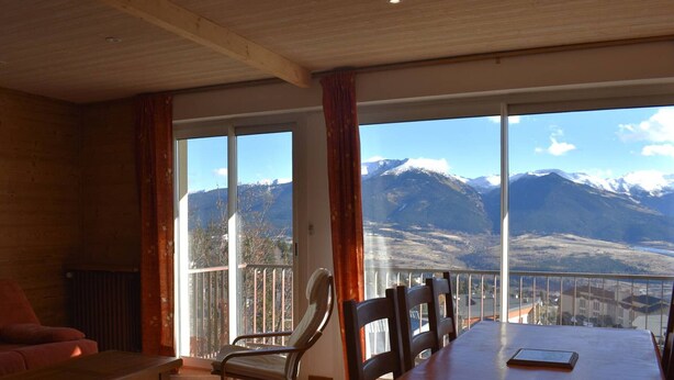 Une pièce dotée d’une grande table et de chaises, d’un canapé et offrant une vue sur les montagnes grâce à de grandes fenêtres.