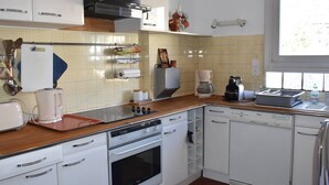 Une cuisine compacte avec des meubles blancs, un four encastré, une machine à café et un lave-vaisselle.