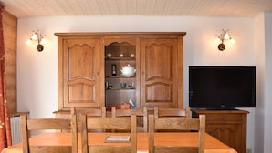 Un coin repas avec une table et des chaises en bois, un meuble avec des étagères et un téléviseur.