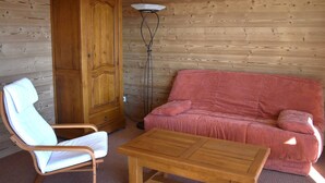 L’intérieur d’un chalet en bois, avec une armoire en bois, une chaise blanche, un canapé rose et une table en bois.