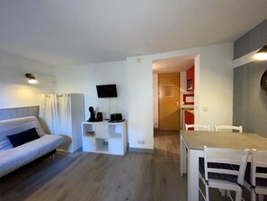 A modern living room with a sofa, a small white table with a TV, and a dining area with chairs and a table.