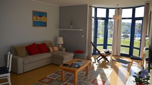 Un soggiorno con divano, tavolino e vista su una piscina attraverso ampie finestre.