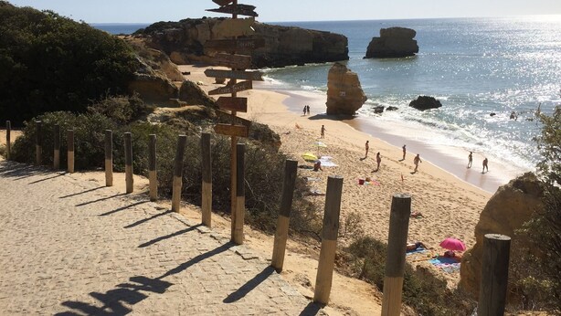 Una spiaggia con un cartello di legno, sabbia dorata e formazioni rocciose.