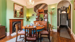 Een eetkamer met een ronde tafel, stoelen, een open haard en een trap naar een andere kamer.