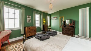 Een slaapkamer met een groot bed, twee kasten, een stoel, een radiator en een raam met gordijnen.