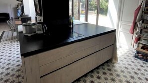 Een moderne keuken met een zwart aanrecht, houten keukenkastjes en een groot raam dat voor daglicht zorgt.