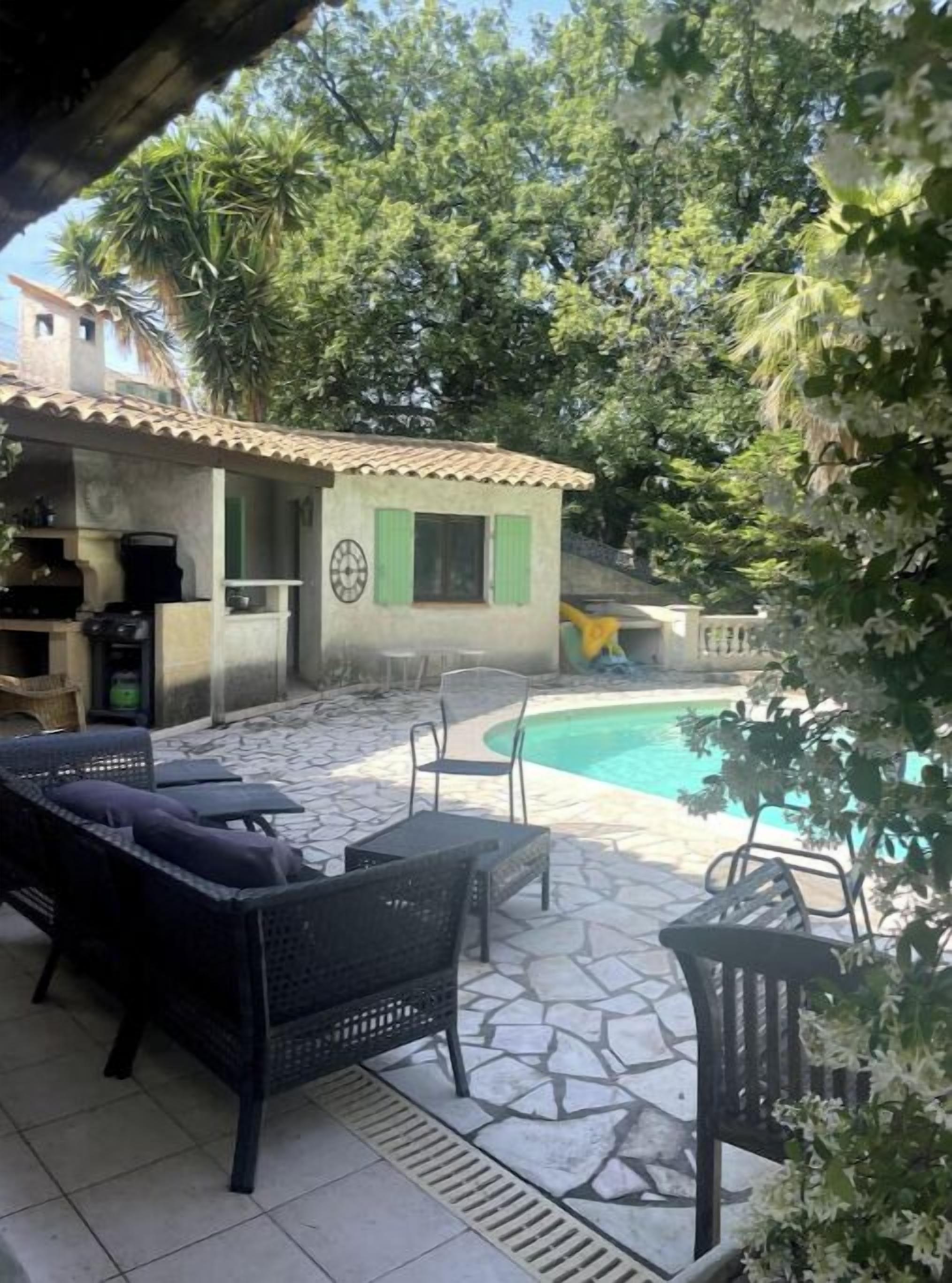 Une terrasse avec des meubles d’extérieur, une piscine et un petit bâtiment doté d’un toit en tuiles.