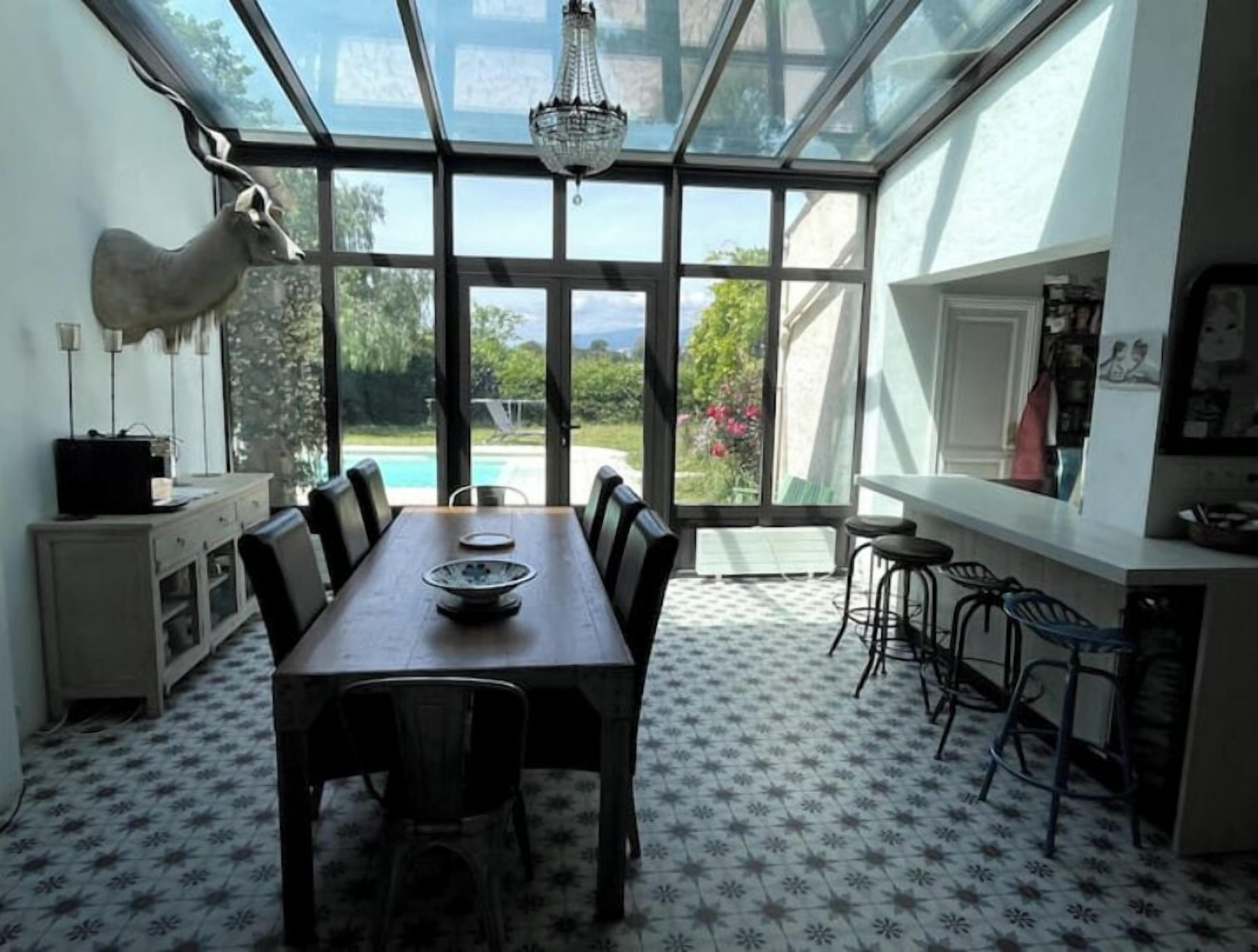 Un espace repas comprenant une grande table, des chaises et une vue sur une piscine, grâce à de larges fenêtres.