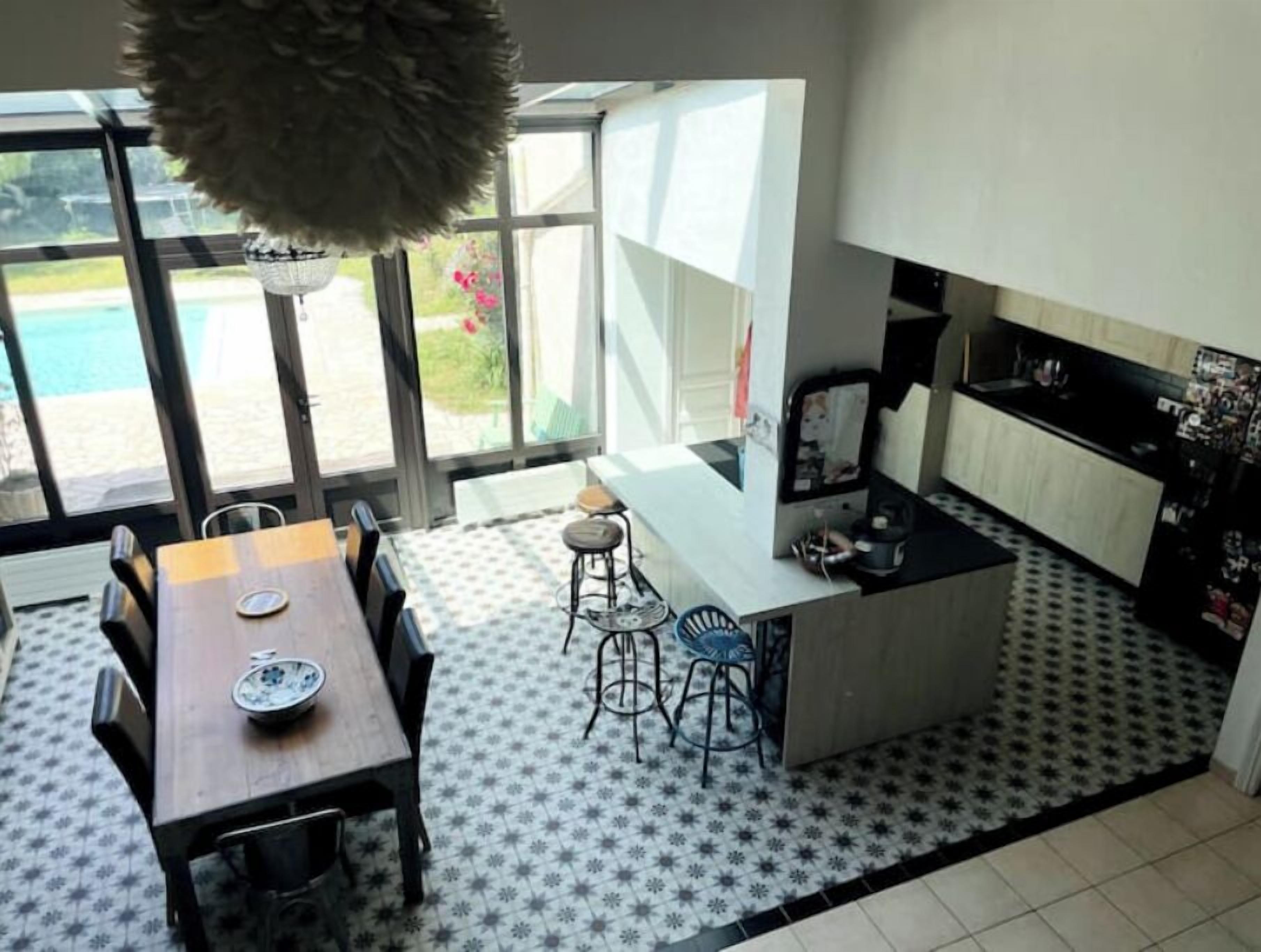 A modern kitchen with a dining area, large windows, and a view of the outdoors.