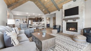 Ein großzügiges Wohnzimmer mit hoher Decke, Kamin und moderner Küche im Hintergrund.