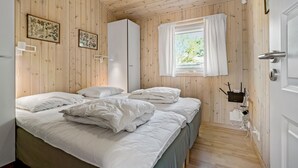 Een slaapkamer met twee bedden, houten wanden, een raam met witte gordijnen en een deur met een moderne deurklink.