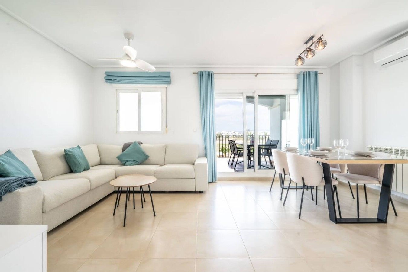 A modern living room with a sofa, a small round table, and a dining area with chairs and a table set for two.