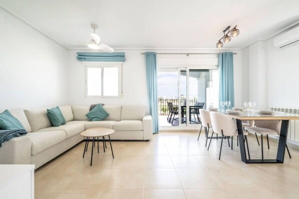 A modern living room with a sofa, a small round table, and a dining area with chairs and a table set for two. - Stunning apartment at La Torre Golf Resort MO6022L (La Torre Golf Resort)