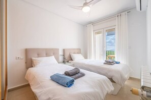 Habitación de hotel con dos camas, ventilador de techo, ventana con cortinas y vista al exterior.