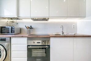 Une cuisine moderne avec des armoires blanches, des appareils en acier inoxydable, un four à micro-ondes et un four encastré.