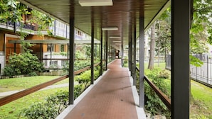 A covered walkway with a brick floor, wooden railings, and a view of a building with balconies and greenery. - Easylife - Refined apartment near the Duomo (Milano)